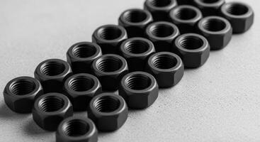 Close up of black metal nuts arranged diagonally on a textured gray surface. photo