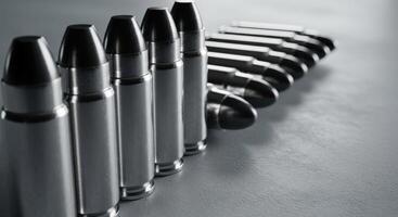 Close up of a row of shiny silver bullets arranged diagonally on a grey surface. photo