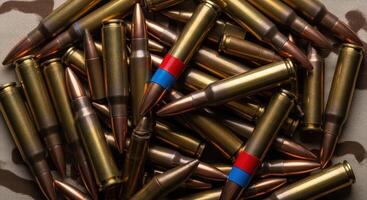 Pile of rifle cartridges with brass casings and copper projectiles on camouflage. photo