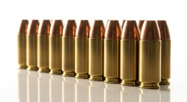 A row of golden bullets with copper tips standing upright on a white reflective surface. photo