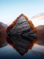Triangular rock formation surrounded by autumn trees in a lake photo