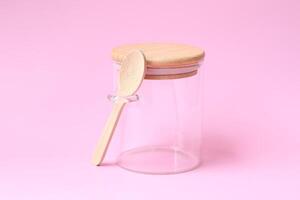 empty glass jar with spoon. on pink background. Side view photo