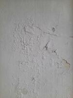Old peeling wall texture with cracked, blistered, and flaking white paint, creating a weathered and distressed surface look. photo