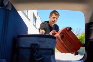 Man loading suitcase into car trunk before travel photo