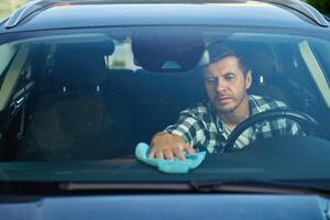 Man cleaning car dashboard from inside of car photo