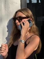 Woman talking on the phone while standing against a wall in bright sunlight photo