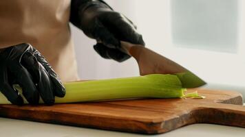 A chef in gloves skillfully chops a stalk of celery on a wooden cutting board. Fresh ingredients emphasize the focus on nutrition and healthy cooking in a modern kitchen setting. video