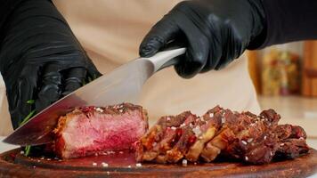 A chef skillfully slices a perfectly cooked steak on a wooden cutting board. Fresh herbs and seasoning enhance the meal's appearance. The kitchen features a clean, eco-friendly layout. video