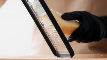 A skilled chef in a minimalistic kitchen grates a block of cheese with precision while wearing black gloves. The focused atmosphere highlights a commitment to healthy cooking and sustainability. video