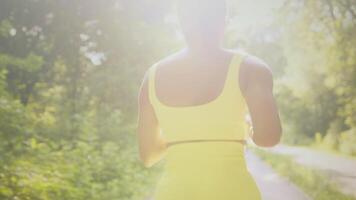 A young African American woman jogs along a serene path in a park, embracing an active lifestyle. Sunlight filters through trees, enhancing the vibrant atmosphere of her run. video