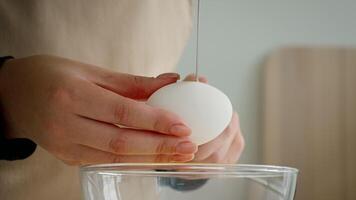 A chef skillfully cracks a fresh egg into a clear glass bowl in a modern kitchen. The focus is on promoting healthy cooking practices with fresh ingredients. video