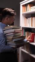 vertical of A man is holding a stack of books in front of a bookcase video