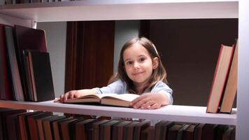 Young girl is immersed in a captivating book, comfortably positioned amidst a vast collection of books on a well-organized bookshelf, showcasing the joy of reading and the importance of literacy video