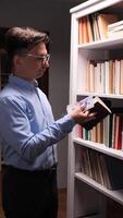 vertical A man in glasses hide money cash into a book is looking at a book shelf video