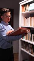 A man in glasses holding a folder in front of a bookcase video