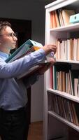 A man in glasses is holding a book in front of a bookcase video