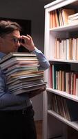 vertical A man is holding a stack of books in front of a bookcase video