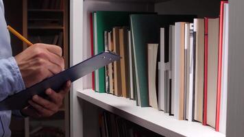 A man is holding a clipboard while standing in front of a book shelf video
