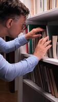 vertical uma homem é olhando às livros em uma estante video