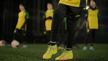 A children's football team trains at the stadium under the guidance of a coach. Kids in sports uniforms practice ball exercises, improve technique, and develop teamwork on the green field 32 video