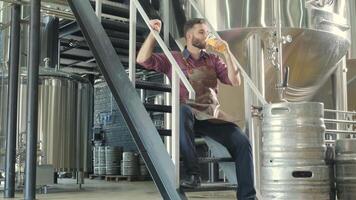 Brewer sitting on keg while checking brewing equipment video