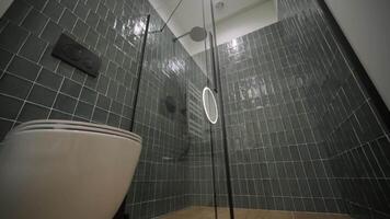 A contemporary bathroom with dark green tiles, an oval mirror with backlighting, a white radiator, and wooden vanity, giving off a modern and functional vibe video