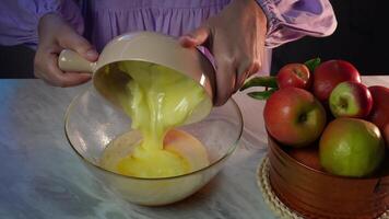 Pouring custard into mixing bowl with fresh apples on table in kitchen setting video
