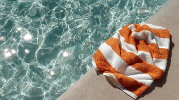 Bright Orange Towel Rests by Serene Pool Reflecting Sunlight on Warm Summer Day. photo