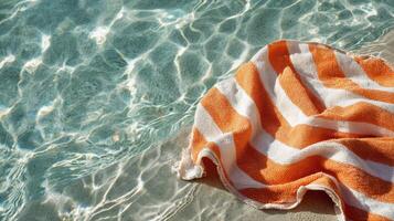 Bright Orange Towel Rests by Serene Pool Reflecting Sunlight on Warm Summer Day photo