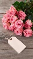 Beautiful Pink Roses Arranged on Wooden Table With Blank Tag for Labeling or Gift Notes. photo
