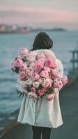 Woman Holding a Large Bouquet of Pink Roses While Standing by the Sea During a Calm Day. photo