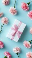 Gift Box Decorated With Pink Ribbon Surrounded by Pink Carnations on Light Blue Background photo