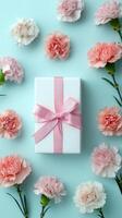 Gift Box Decorated With Pink Ribbon Surrounded by Pink Carnations on Light Blue Background. photo