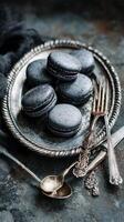 Elegant Black Macarons Arranged on a Vintage Silver Platter With Silverware on a Rustic Table photo