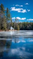 Winter Cabin Reflection Over Frozen Lake With Pine Trees and Clear Blue Sky photo
