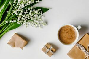 Coffee Cup and Wrapped Gifts Surrounded by Lily of the Valley on White Surface in Morning Light photo
