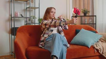 Pretty female girl blogger looks at device screen taking selfie on mobile cell phone cam, make virtual call online on modern social media vlog application. Woman with smartphone on sofa at home video