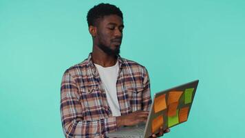 Exhausted african american man freelancer with pasted sticker notes use laptop computer having concentration problem creative crisis. Nervous guy confused by big routine work loading. Blue background video