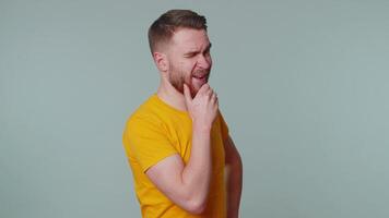 Smiling playful happy stylish man in casual t-shirt blinking eye, looking at camera with toothy smile, winking and flirting, expressing optimism. Young handsome adult guy alone on gray wall background video