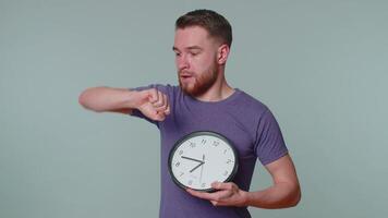 Confused young man with anxiety checking time on clock, running late to work, being in delay, deadline on gray studio background. Serious guy looking at hour and minutes, worrying to be punctual video
