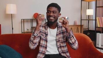 Man freelancer holding two gold coins at home, successful developer programmer. Guy stock trader earning bitcoins after online monitoring trading operations. Increasing wealth, financial prosperity video