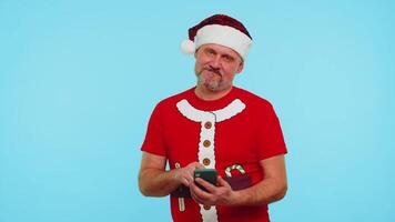 Man in Christmas t-shirt and hat using mobile phone typing new post on web, sms message, browsing, addiction of social networks, showing thumbs up. Happy New Year celebration holidays shopping online video