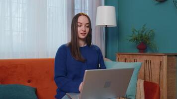 Young woman with headset using laptop pc, talking, working customer support service operator at home office, in headphones with microphone in living room. Coronavirus quarantine distance isolation video
