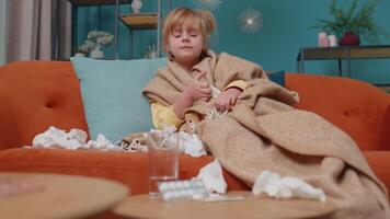 Portrait of Caucasian child girl suffering from cold or allergy in plaid lying on sofa in living room at home. Sick school toddler kid with runny nose, sneezes snot into napkin. Coronavirus pandemic video
