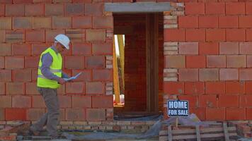 Professional builder engineer architect analyzes blueprints and dimensions at construction site porch. Foreman worker wearing hard hat and vest at building house. Business, real estate, investment video