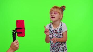 Cheerful funny little teen girl kid dancing at camera filming using phone at home on chroma key background. Schoolgirl child creating her trendy content on a mobile app to share on social media video