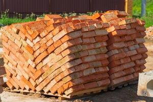 Stack of red clay brick on construction site. Bricks pallet. Red brick for building a house. Construction Materials photo