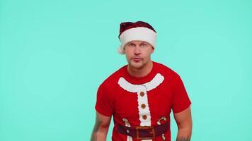 Countdown to holiday celebration. Joyful man wearing red t-shirt Santa Christmas hat counting in reverse order from three to one on blue studio background. Win scream, winner gesture. Happy New Year video