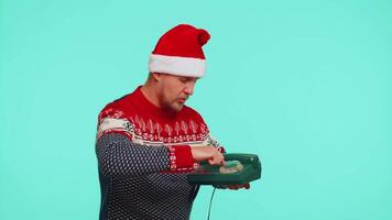 Hey You, call me back. Funny man in red Christmas sweater talking on wired vintage telephone of 80s, says hey you call me back on blue studio wall background. Happy New Year celebration merry holiday video