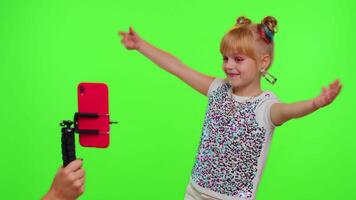 Young Blogger Concept. Cheerful teen school girl kid dancing at camera filming using phone at home on chroma key background, creating her trendy content on a mobile app to share on social media video
